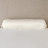 Paloma Throw Pillow | Parchment | bolster on white sheets with a neutral headboard.