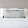 Paloma Throw Pillow | Eucalyptus | 16x36 charmeuse pllow wth silk velvet trim against white sleeping pillows and sheets — straight on with neutral background.