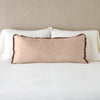 Paloma Throw Pillow | Rouge | 16x36 charmeuse pllow wth silk velvet trim against white sleeping pillows and sheets — straight on with neutral background.