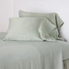 Paloma Pillowcase (Single) | Eucalyptus | sleeping pillows leaning upright against a white wall on monochromatic sheeting - cropped three-quarter angle.