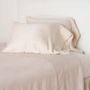 Paloma Pillowcase (Single) | Pearl | sleeping pillows leaning upright against a white wall on monochromatic sheeting - cropped three-quarter angle.