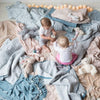 Silk Velvet Quilted Baby Blanket | Two babies sitting and playing on a floor covered with rumpled blankets in a variety of textures of blue, grey, and pink tones - overhead view.