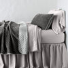 Silk Velvet Quilted Blanket | Fog | throw blanket rumpled and folded back, featuring satin back. Shown with matching lumbar pillow and monochromatic sheeting - side view.
