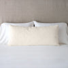 Vienna Throw Pillow | Parchment | 16x36 pillow leaning upright against white sleeping pillows on a neutral headboard.