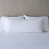 Vienna Throw Pillow | White | 16x36 pillow leaning upright against white sleeping pillows on a neutral headboard.