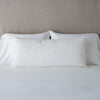 Vienna Throw Pillow | Winter White | 16x36 pillow leaning upright against white sleeping pillows on a neutral headboard.