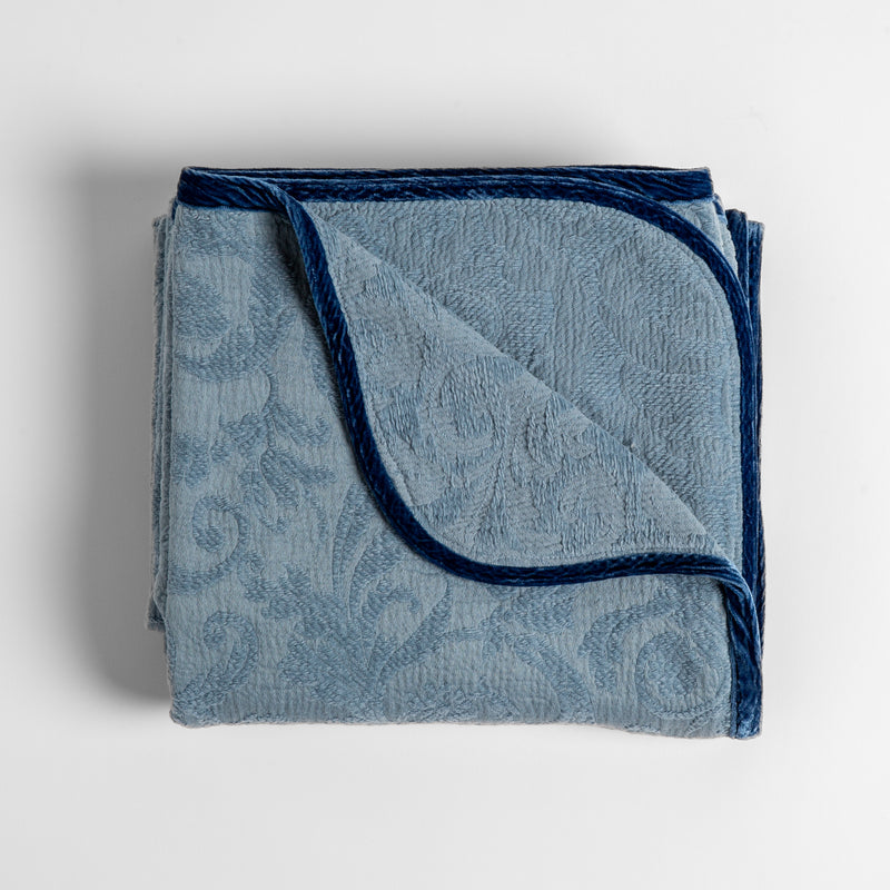 Adele Blanket | Tahoe Blue | folded organic cotton damask throw blanket shown with the corner folded down to show silk velvet trim detail — overhead against a plain white background.