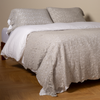 Allora Bed Scarf | Cloud | cotton lace bed scarf draped across the foot of a bed dressed in linen sheets and duvet cover in winter white -  shown with matching lace pillowcase covers over a linen liner in winter white.