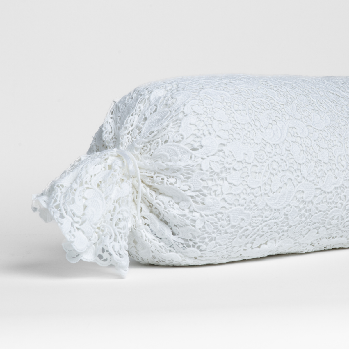 White:  one end of a lace boslter cover on a winter white liner against a white background. 
