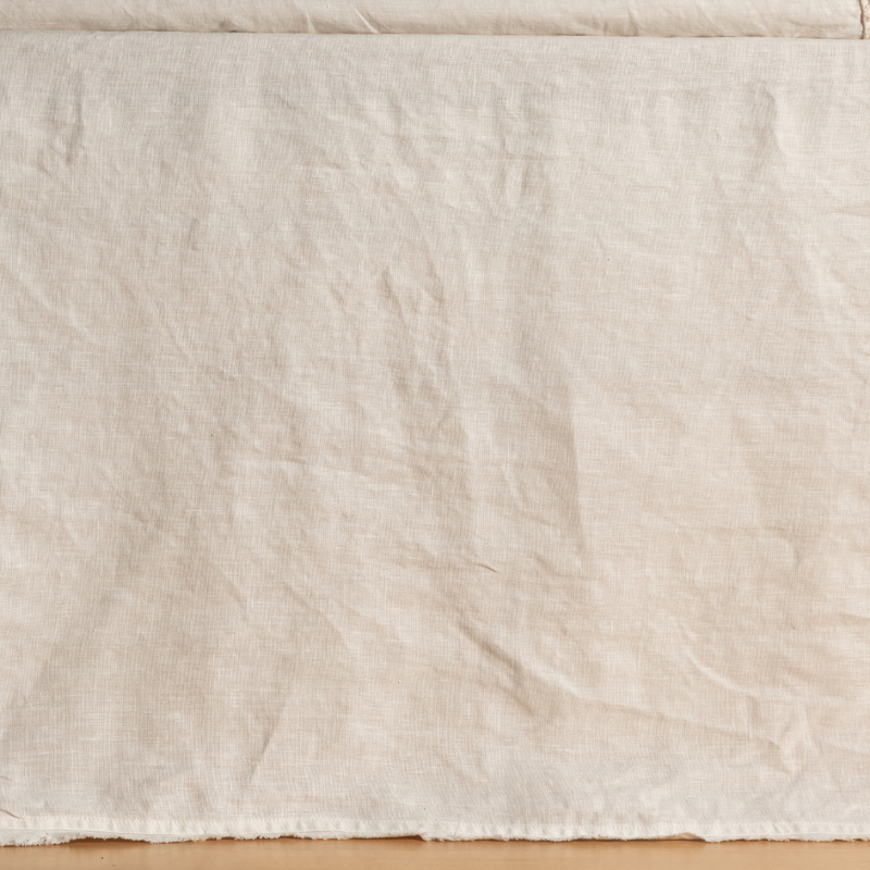Austin Bed Skirt | Natural | a midweight linen bed skirt in natural, the raw edge skimming a wooden floor.