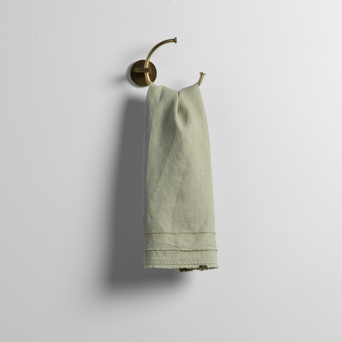 Austin Guest Towel | Desert Sage | a linen guest towel on a decorative towel ring in desert sage, a serenely elegant green, offering a hushed hue, shown against a plain background.