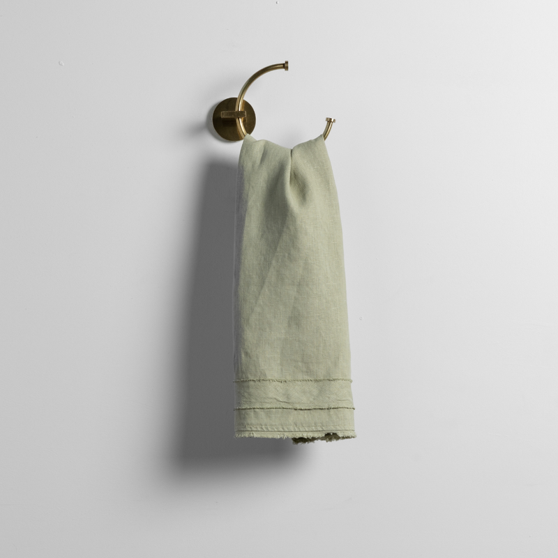 Austin Guest Towel | Desert Sage | a linen guest towel on a decorative towel ring in desert sage, a serenely elegant green, offering a hushed hue, shown against a plain background.