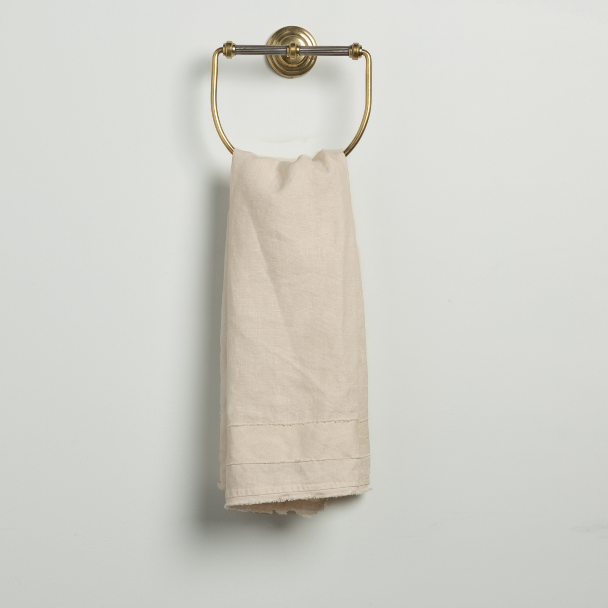 Austin Guest Towel | Natural | a midweight linen guest towel on a brass towel ring against a plain background.