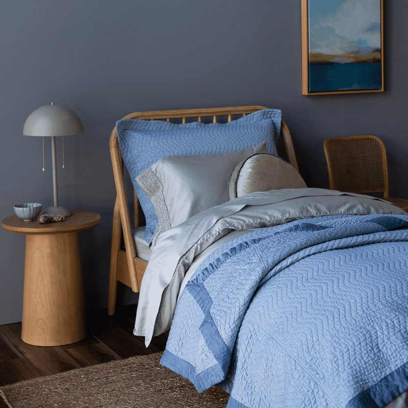 Cirillo Twin Coverlet | a twin bed shown from an angle dressed mostly in monochromatic tones, the flat sheet is folded back over the duvet cover which is pulled back over the coverlet.
