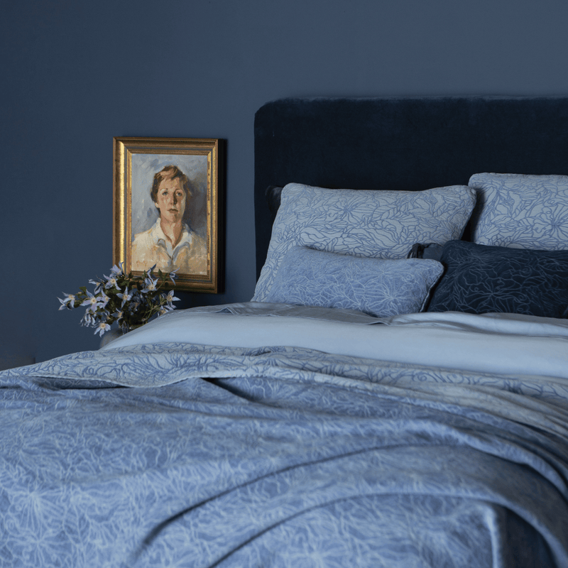 Georgia Bedspread | a three-quarter view of a fully dressed bed in blue tones with a velvet headboard against a blue wall.