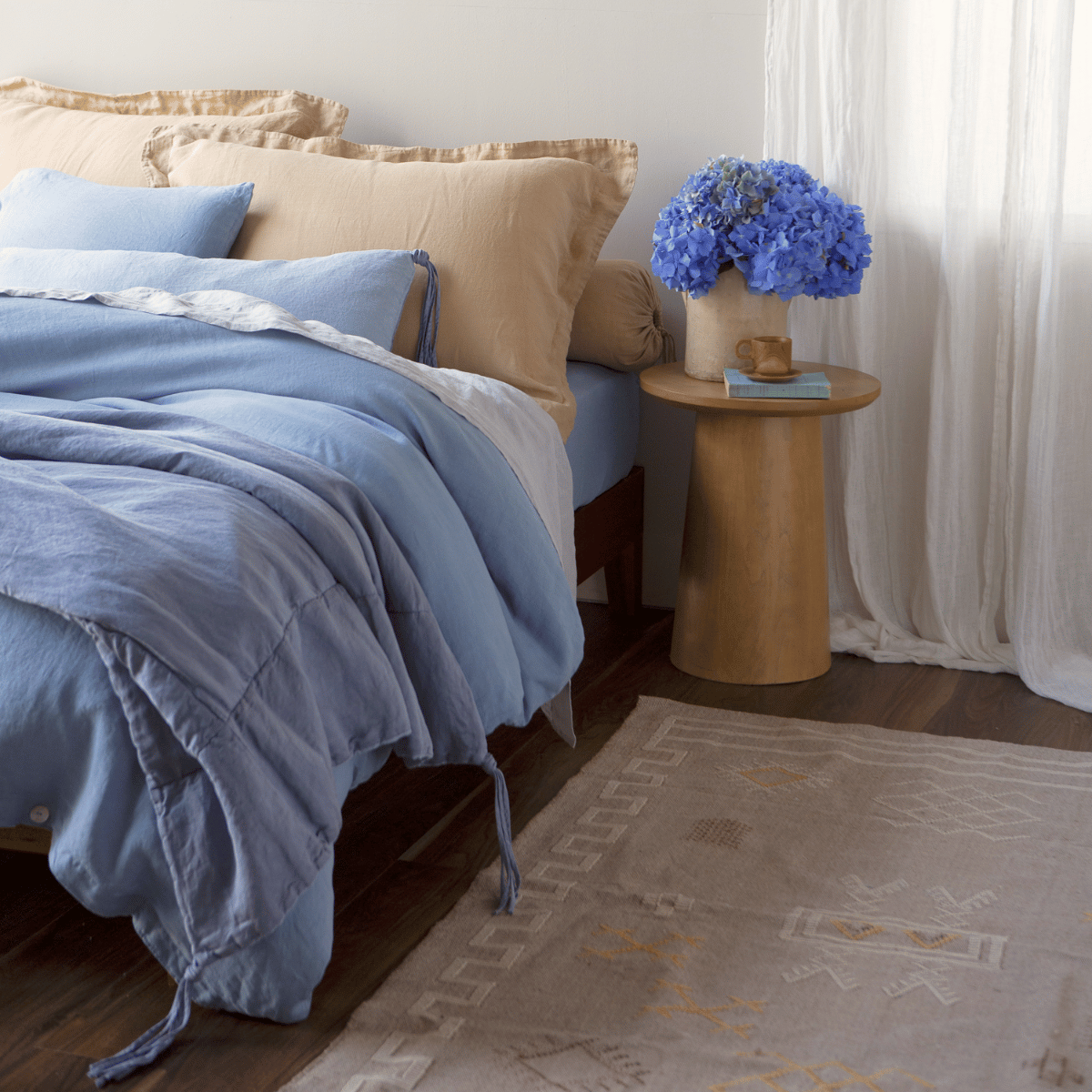 Linen Duvet Cover | a bed dressed in mostly linen  in blue and golden tones that match the flowers and side table.