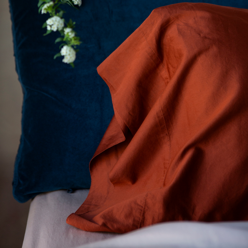Bria Pillowcase (Single) | a close up of a cotton sateen pillowcase in autumn, a rich terracotta tone, against a sham in midnight, a dark blue hue.