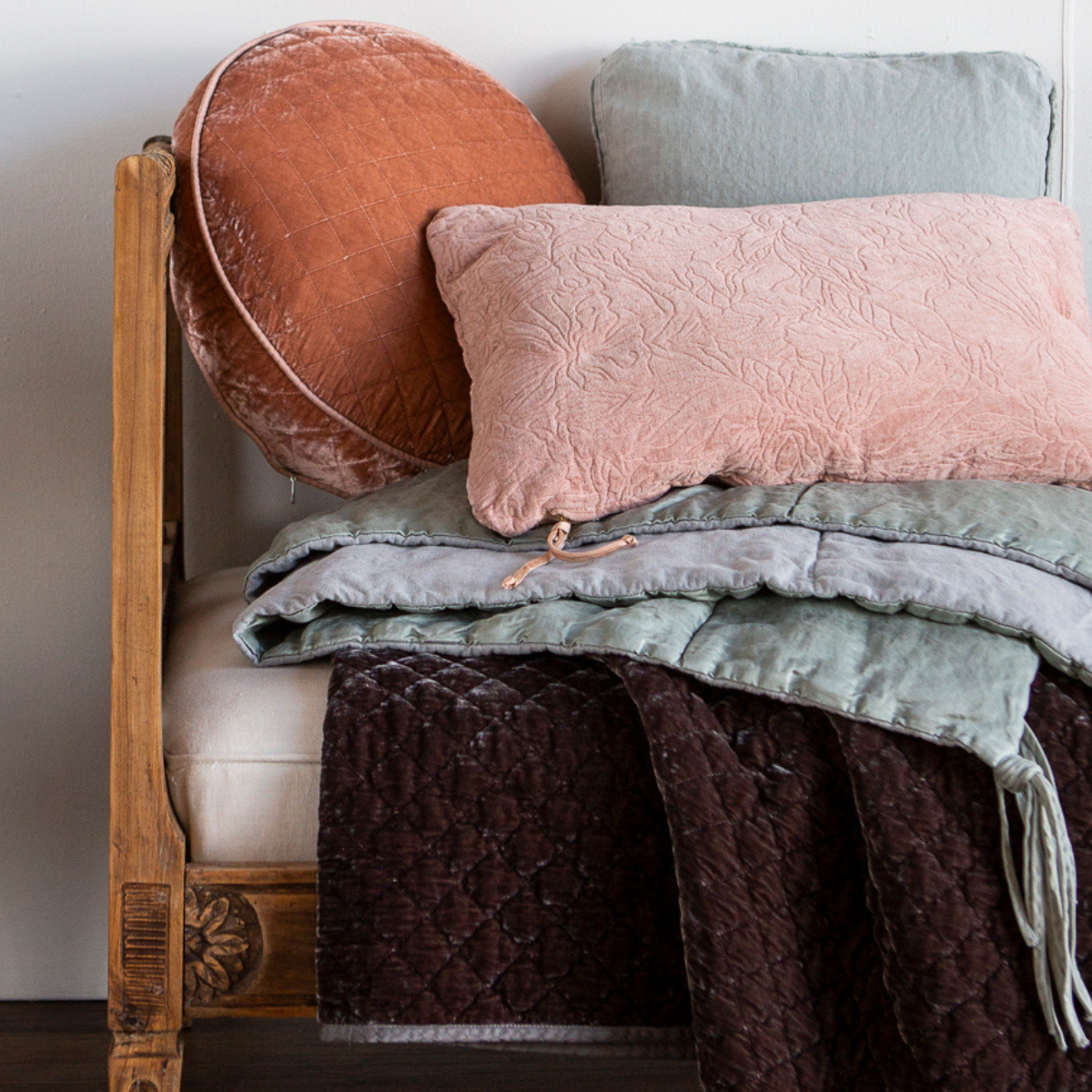 Georgia Throw Pillow | A close up of one side of a daybed bench styled with throw pillows and throw blankets in grey, light green and warm tones.