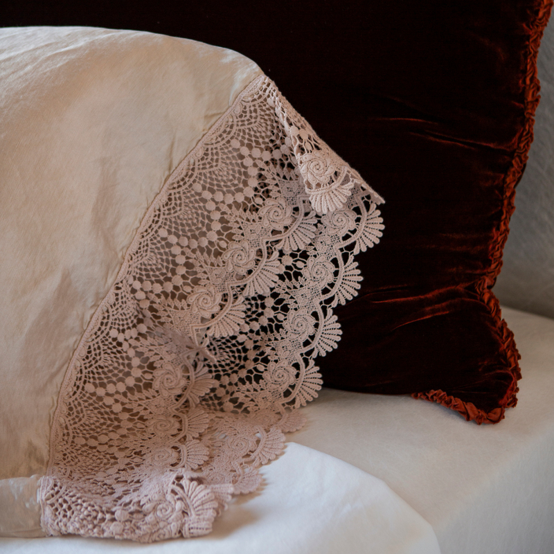 Paloma Pillowcase (Single) | Pearl | A close up of mattine lace trimmed charmeuse pillowcase against a silk velvet sham in a dark rusty tone.