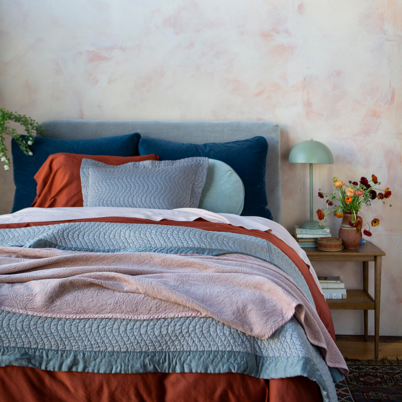 Georgia Blanket | a light pink blanket at the foot of a dressed bed in light green, rust and dark blue tones.