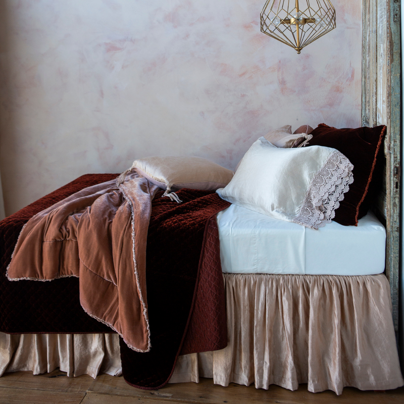 Silk Velvet Quilted Coverlet | a quilted silk velvet coverlet shown with matching shams and other bedding in pink and whtie tones - shown from the side view against a pink toned wall.