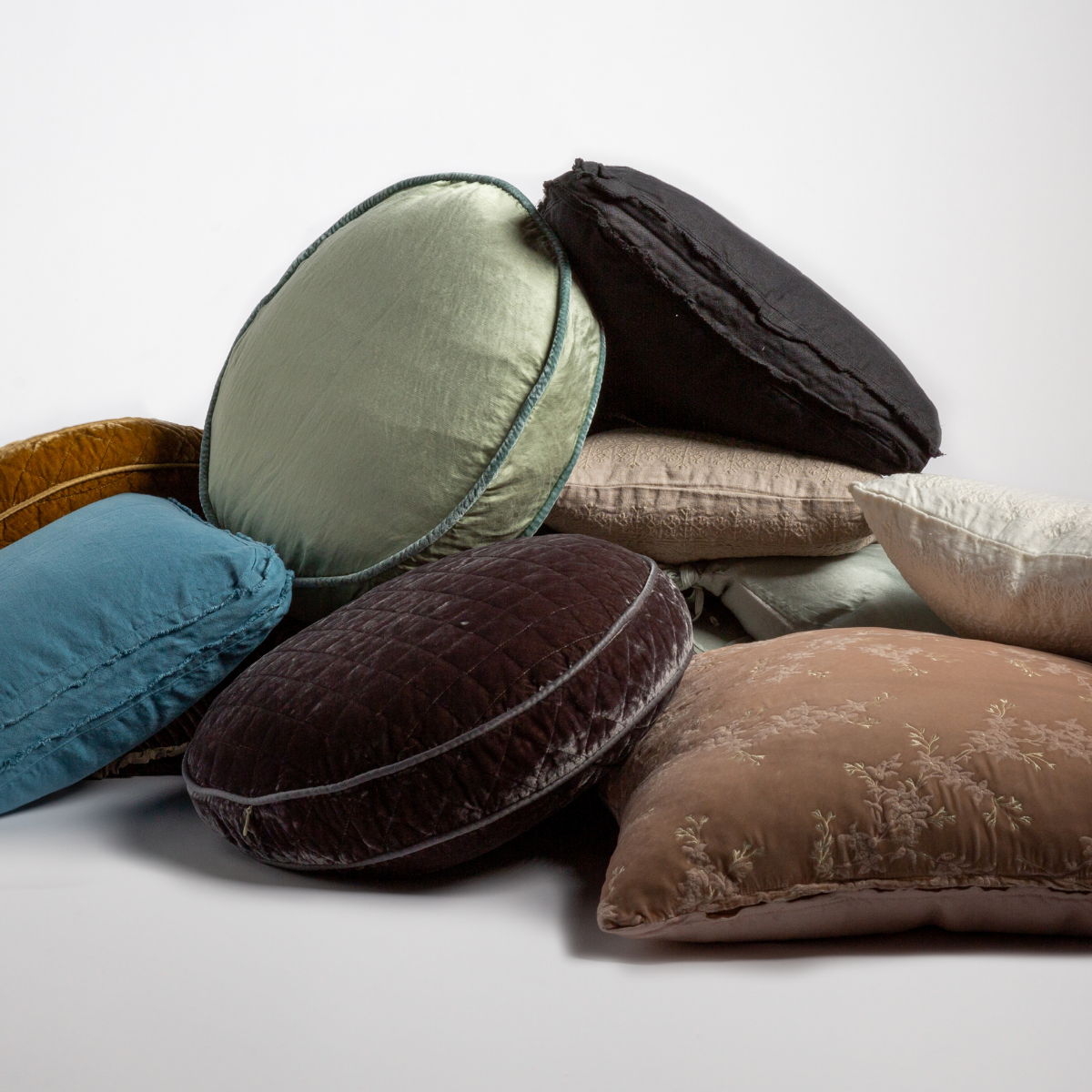 Renewal | A stack of several throw pillows in different colors and fabrics shown against a white background. 