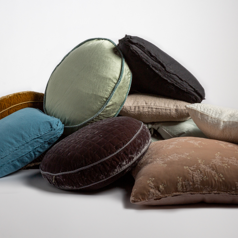 Renewal | A stack of several throw pillows in different colors and fabrics shown against a white background. 