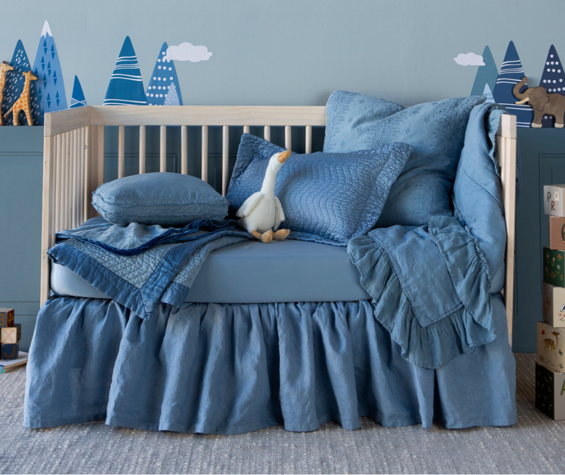 Linen Crib Skirt | an all-blue crib styled as a toddler bed with toys scattered about the scene and tree decals on the wall.