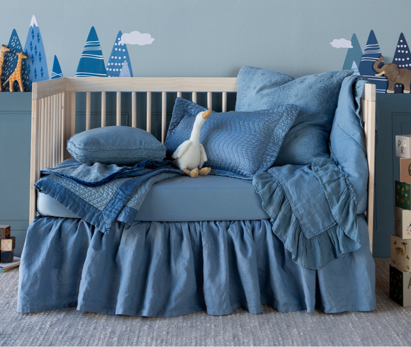 Linen Crib Skirt | an all-blue crib styled as a toddler bed with toys scattered about the scene and tree decals on the wall.