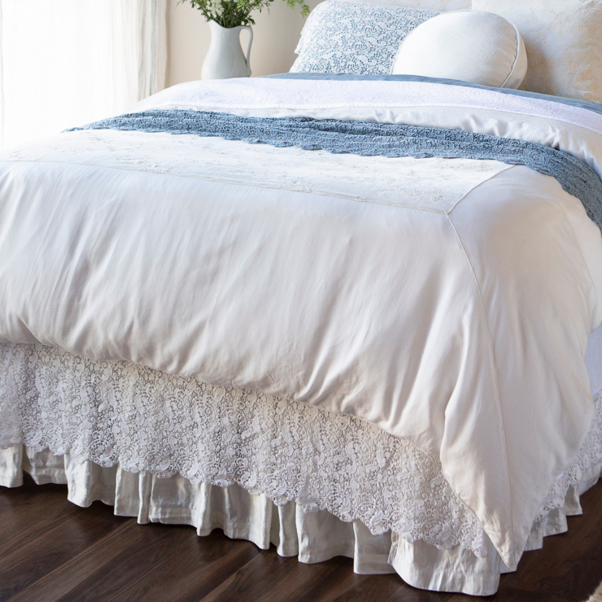 Allora Bed Skirt | a lace bed skirt layered over a charmeuse bed skirt on a bed dressed in whites and blue.