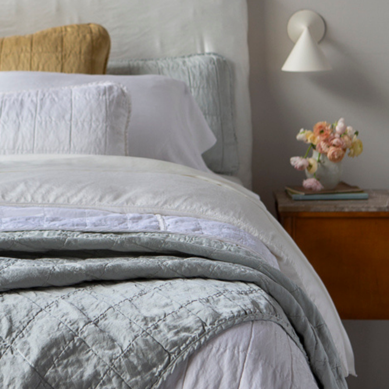 Sel Blanket | Shot from the foot of the bed, a quilted charmeuse blanket is in the foreground and the pillows at the head of the bed are slightly out of focus.