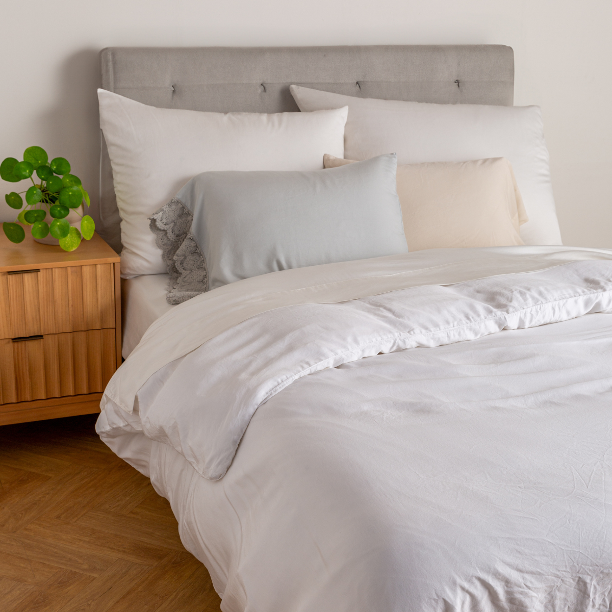 Madera Luxe Duvet Cover | a bed dressed in pieces from the madera luxe collection in light and neutral tones, with a grey headboard and side table with plant.