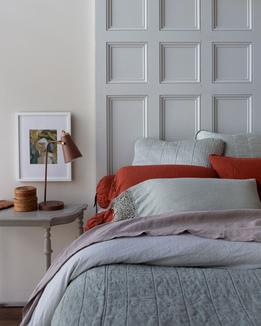 A lightly dressed bed that mixes our existing fabrics with our new Sel collection. A pop of Autumn sits against an earthy-toned bed. Light gray bed sore-able with brown decor ontop sits next to the bed. 