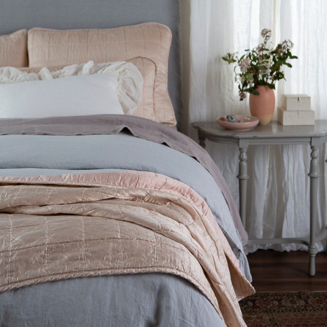 Sel Blanket | shot from the foot of the bed, a quilted charmeuse blanket is in the foreground and the shams and decorative throw pillows slightly out of focus at the head of the bed.