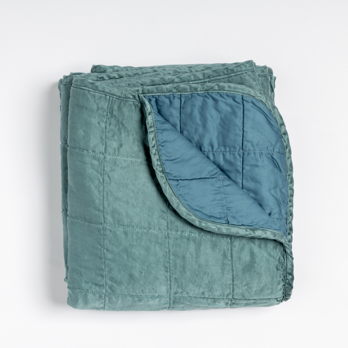 Sel Blanket | Cenote | an overhead shot of a quilted charmeuse blanket in cenote, a vibrant ocean-inspired blue-green, with a corner folded down, showing its cotton sateen back.