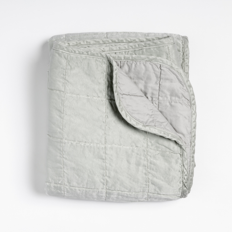 Sel Blanket | Cloud | an overhead shot of a quilted charmeuse blanket in cloud, a subtle sky blue-grey, with a corner folded down, showing its cotton sateen back.