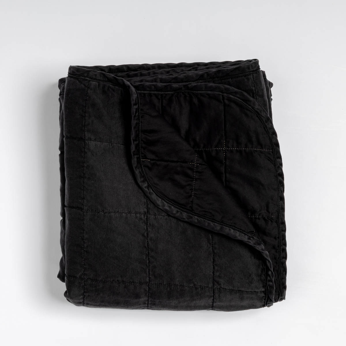 Sel Blanket | Corvino | an overhead shot of a quilted charmeuse blanket in corvino, our classic black, with a corner folded down, showing its cotton sateen back.