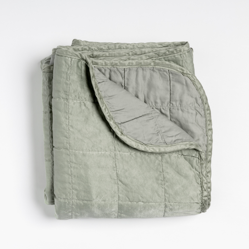 Sel Blanket | Eucalyptus | an overhead shot of a quilted charmeuse blanket in eucalyptus, a soft light green, with a corner folded down, showing its cotton sateen back.
