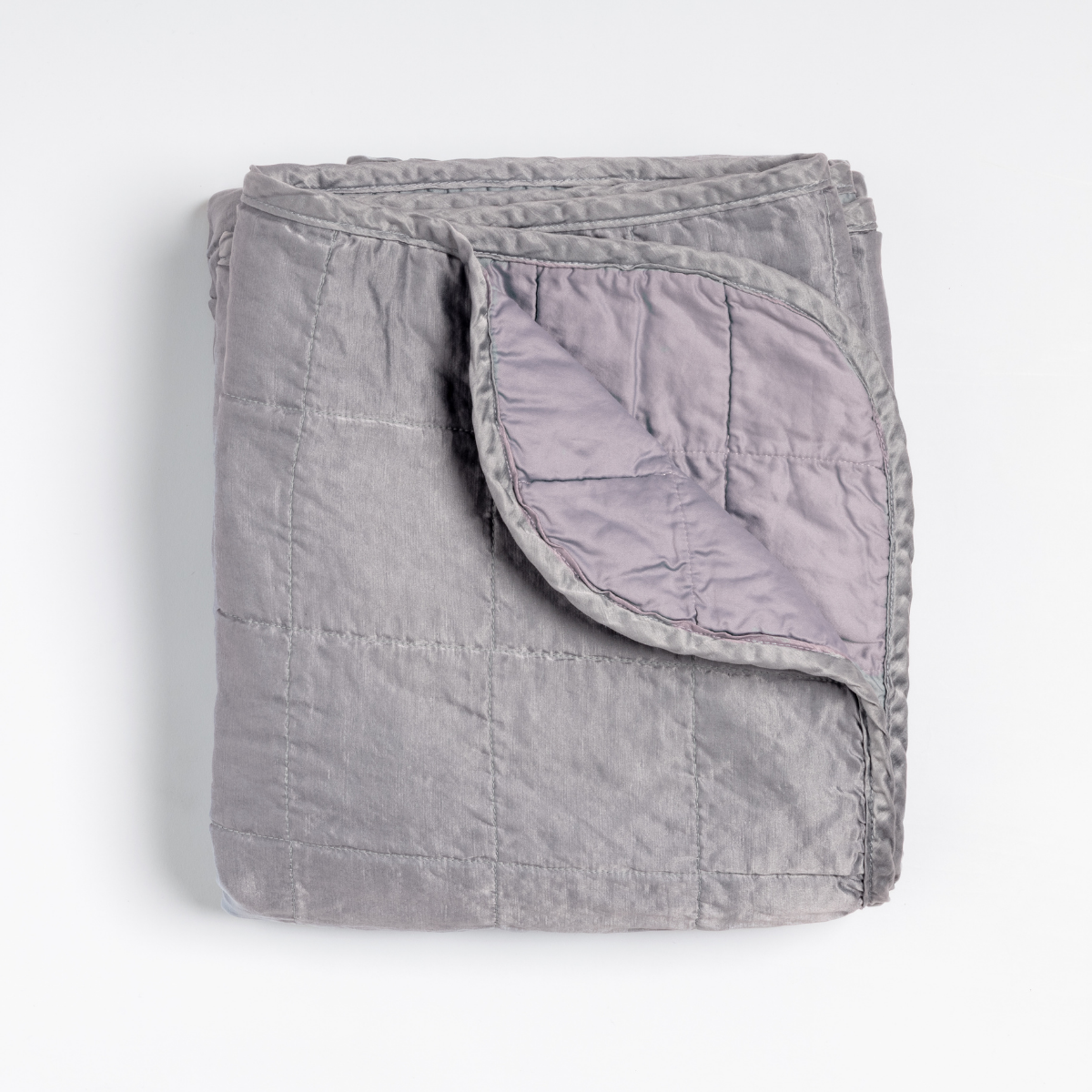 Sel Blanket | French Lavender | an overhead shot of a quilted charmeuse blanket in french lavender, a neutral violet tone, with a corner folded down, showing its cotton sateen back.