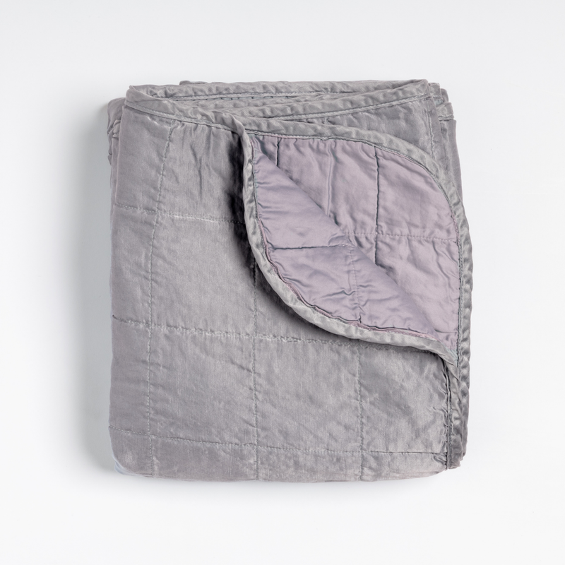 Sel Blanket | French Lavender | an overhead shot of a quilted charmeuse blanket in french lavender, a neutral violet tone, with a corner folded down, showing its cotton sateen back.