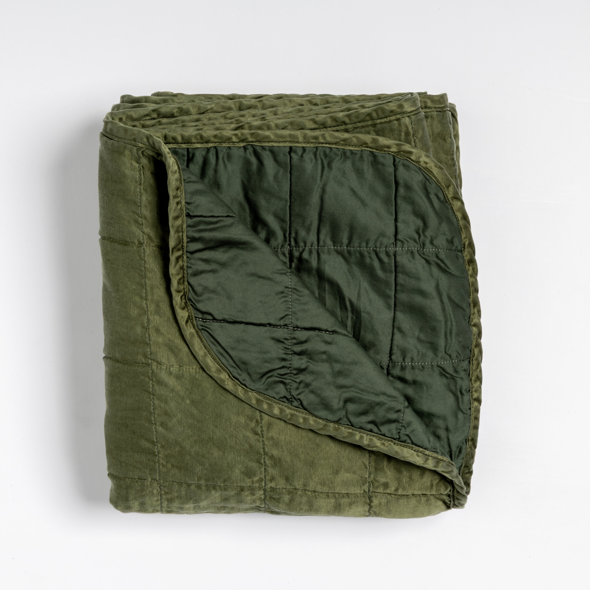Sel Blanket | Juniper | an overhead shot of a quilted charmeuse blanket in juniper, a deeply saturated dark green, with a corner folded down, showing its cotton sateen back.