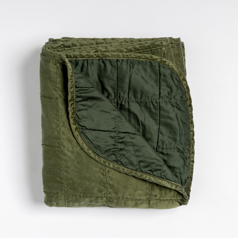 Sel Blanket | Juniper | an overhead shot of a quilted charmeuse blanket in juniper, a deeply saturated dark green, with a corner folded down, showing its cotton sateen back.