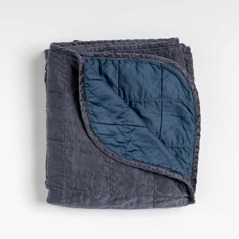 Sel Blanket | Midnight | an overhead shot of a quilted charmeuse blanket in midnight, a rich indigo tone, with a corner folded down, showing its cotton sateen back.