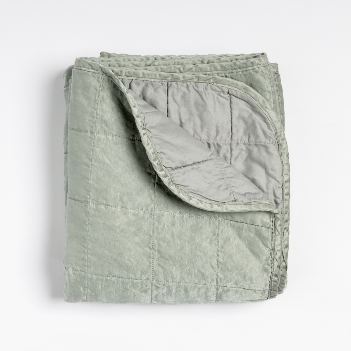 Sel Blanket | Mineral | an overhead shot of a quilted charmeuse blanket in mineral, a soothing seafoam blue with subtle grey-green undertones, with a corner folded down, showing its cotton sateen back.