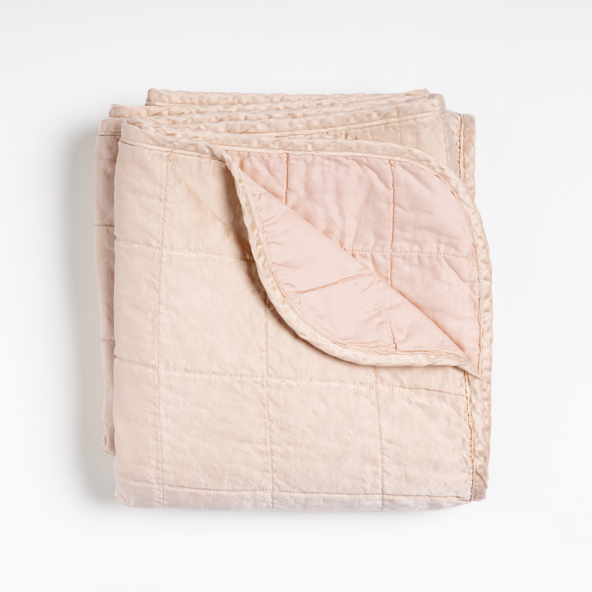 Sel Blanket | Pearl | an overhead shot of a quilted charmeuse blanket in pearl, a soft rose pink tone, with a corner folded down, showing its cotton sateen back.
