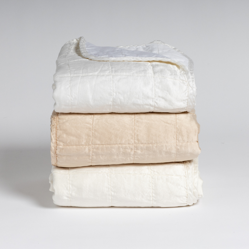 Sel Blanket | A stack of three square-quilted charmeuse blankets shot straight on against a white background. Colors from top to bottom are White, Pearl, and Winter White.