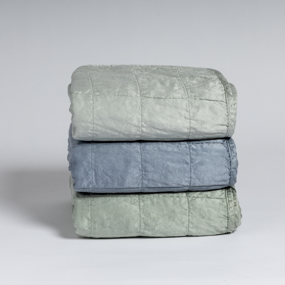 Sel Blanket | A stack of three square-quilted charmeuse blankets shot straight on against a white background.