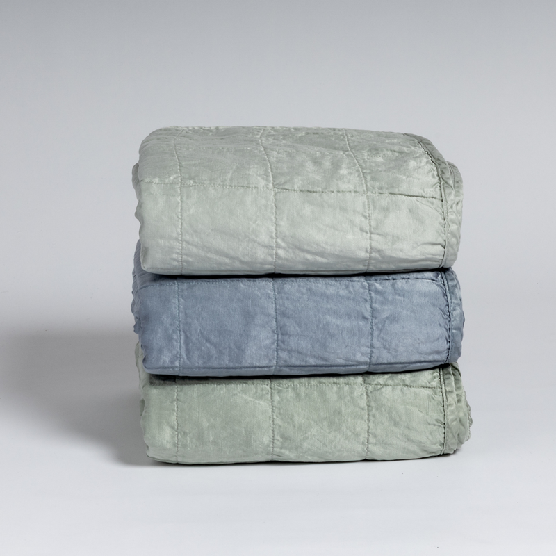 Sel Blanket | A stack of three square-quilted charmeuse blankets shot straight on against a white background.