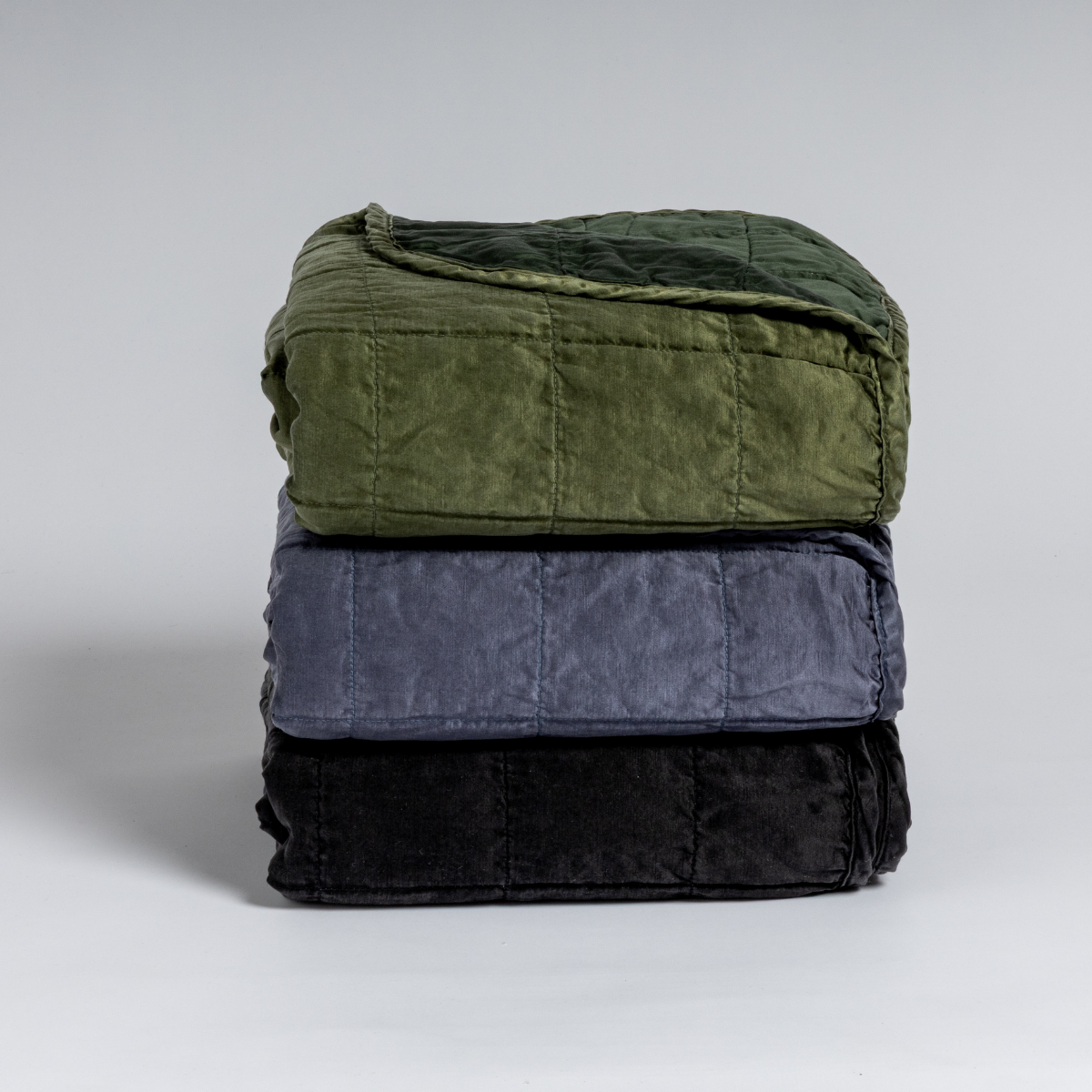 Sel Blanket | A stack of three square-quilted charmeuse blankets shot straight on against a white background. 