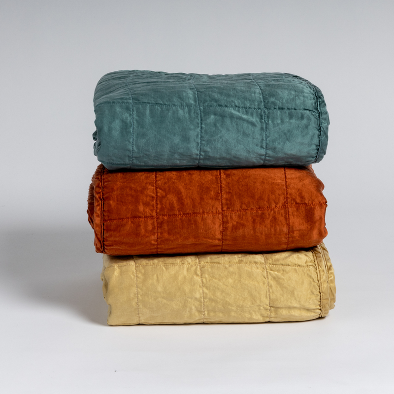 Sel Blanket | A stack of three square-quilted charmeuse blankets shot straight on against a white background. 